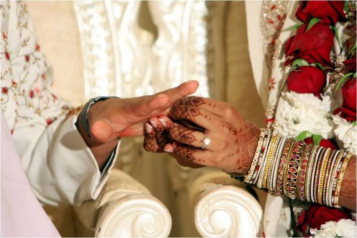 Indian groom slips wedding band on beautiful bride’s finger during traditional wedding ceremony