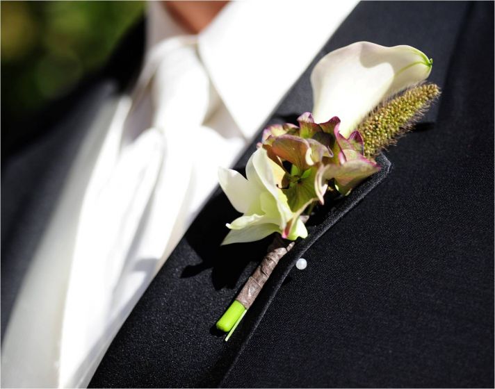 Groom wears traditional black tux and white shirt & tie, unique boutinierre