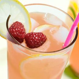 Pink lemonade in a tall glass, garnished with lemon and raspberries.