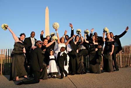 Bride, groom, entire wedding party jump up outside in front of local monument