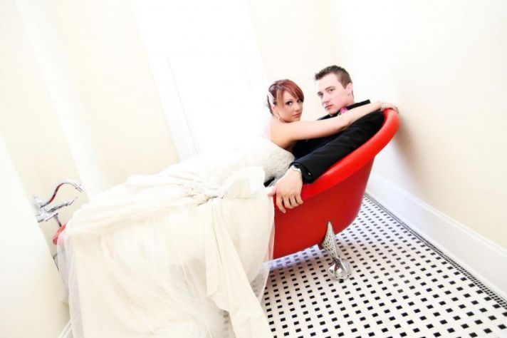 Bride and groom pose in red, vintage bath tub, black and white checkered floor