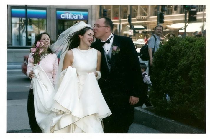 The groom gives the beautiful bride in her sleeveless white wedding dress a kiss on the forehead.