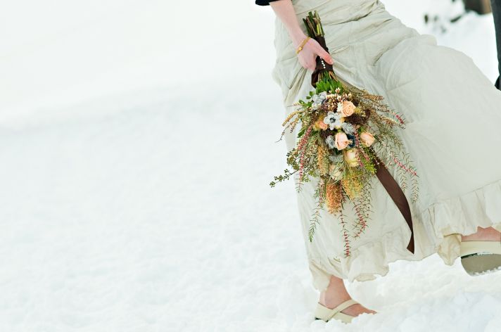 Winter wedding bride holds inventive bridal bouquet which includes paper flowers made from pages of 