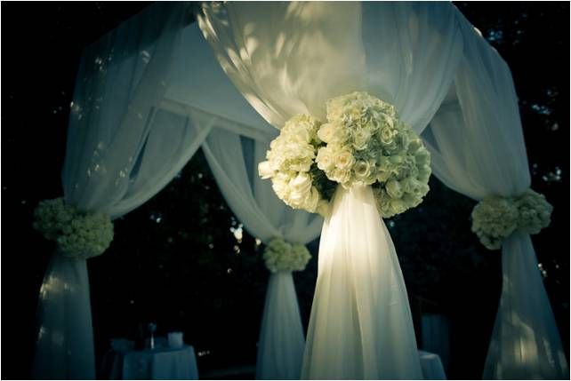 Ivory chuppah adorned with ivory roses for this chic outdoor wedding ceremony