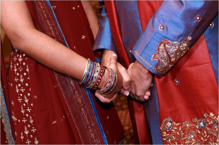 Indian bride and groom, wearing traditional colors of blue, red and gold, gold hands after saying I 