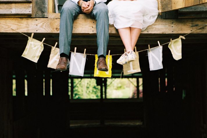 Casual bride and groom pose outside wedding venue with custom wedding monogram sign