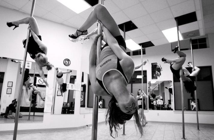 Black, white photo of bride and bridesmaids hanging upside down on poles during pole dancing lessons
