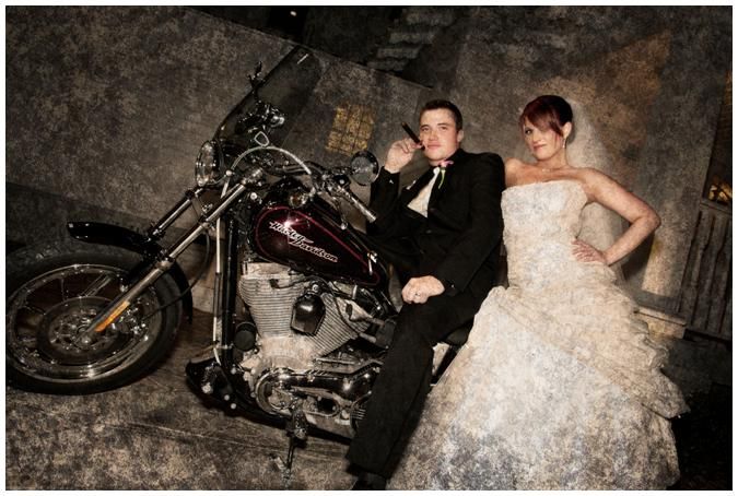 Bride, in white strapless wedding dress, and groom pose on Harley Davidson