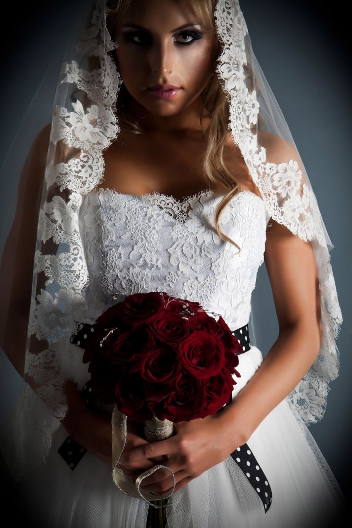 Stunning white lace strapless wedding dress with black and white sash.� Bride holds deep red bridal 