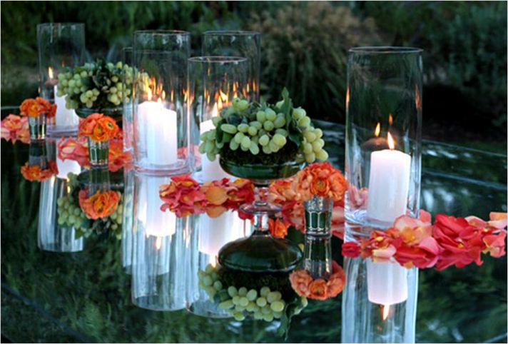 Bright orange and coral rose petals strewn on mirrored reception table; accented with green grapes a