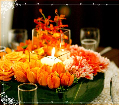 Beautiful low centerpiece- orange flowers surround glass votice holder and candle