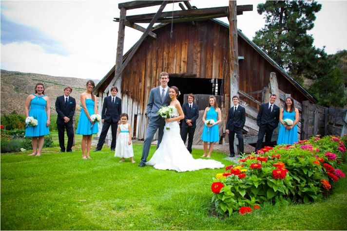 Bride and groom pose outside of rustic wedding venue with wedding party