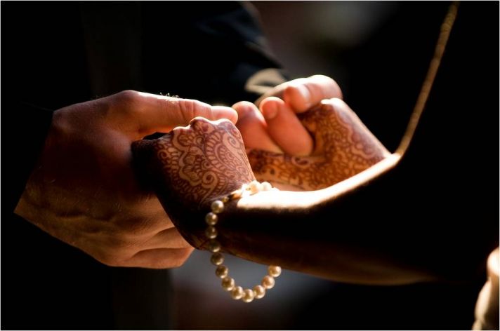 Bride’s henna-adorned hands are placed in groom’s hands while taking their vows