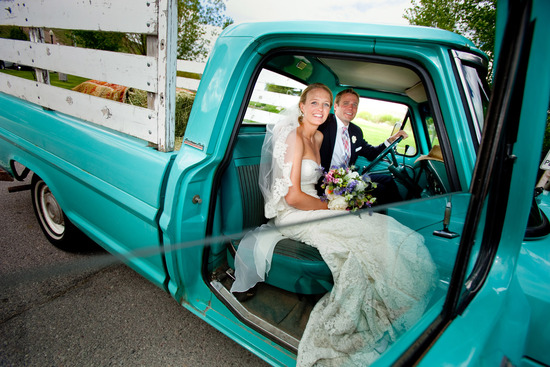 Bride and groom smile as they head to wedding reception in vintage pickup truck