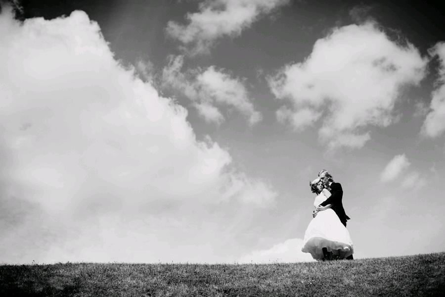 A-castle-wedding-european-romantic-black-and-white-wedding-photo-groom-holds-bride-outside-atop-hill-clouds-sky-in-background.full