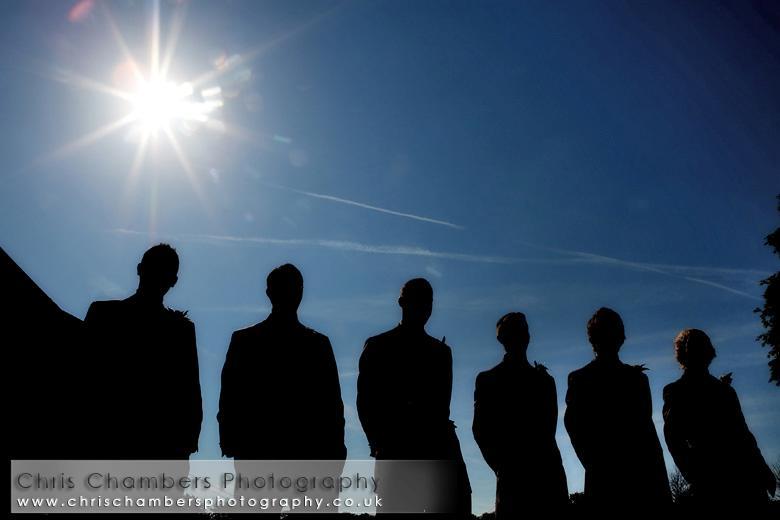 Shadow-of-groom-and-groomsmen-in-tuxes-stand-outside-blue-sky-bright-sun-shining.full